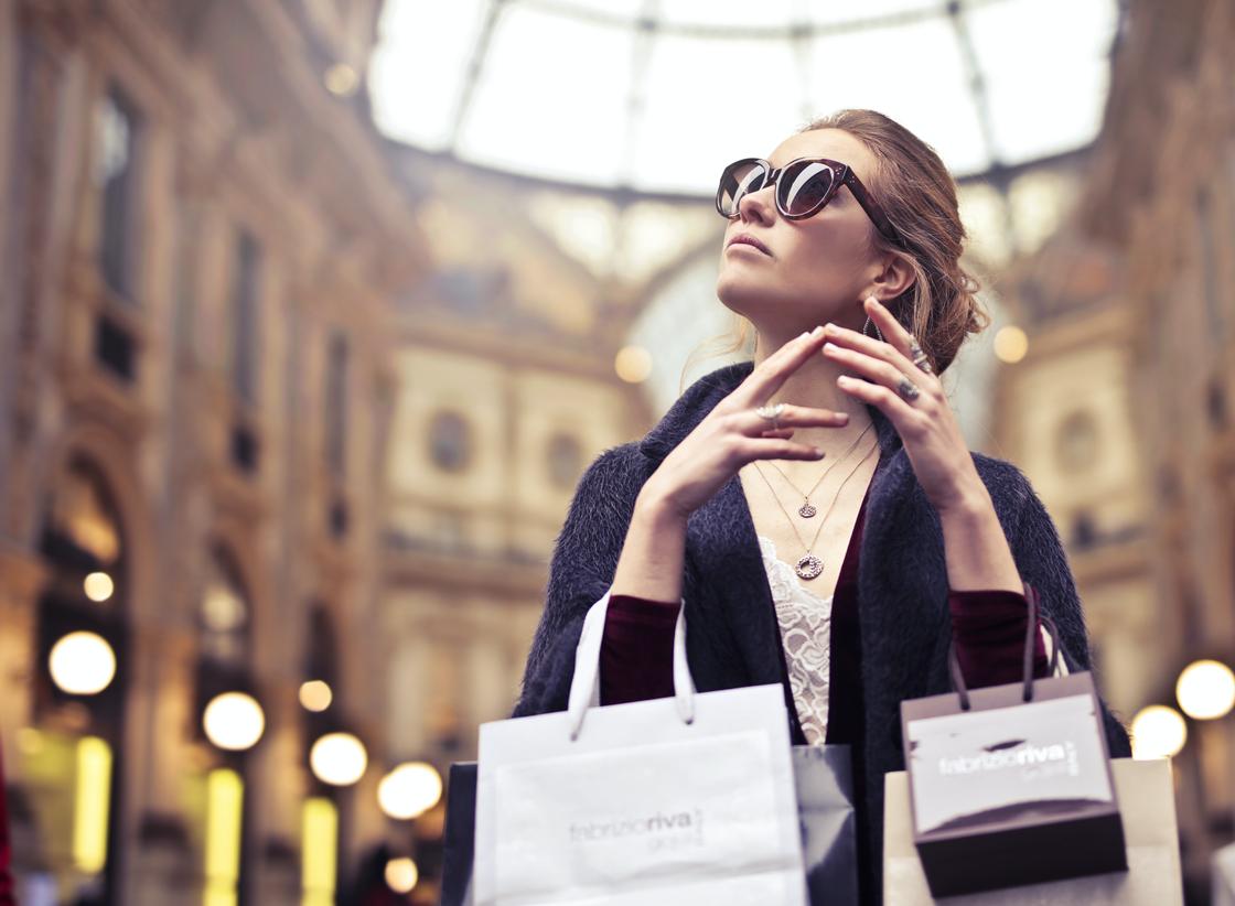 Стильно одетая женщина в солнцезащитных очках держит пакеты с покупками