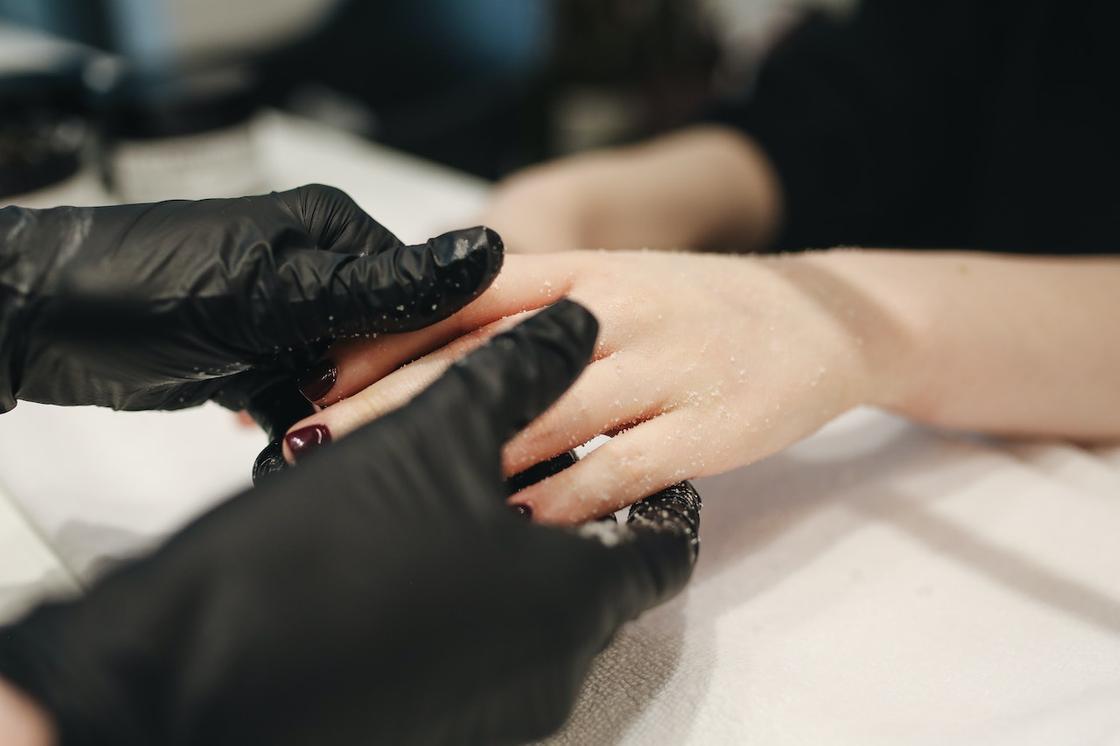 Мастер в черных перчатках проводит скрабирование рук