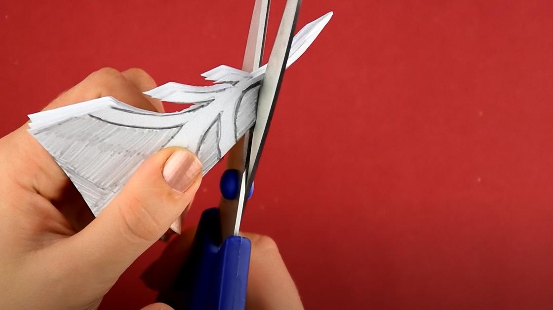 Ножницами вырезают узор на сложенном слоями бумажном треугольнике