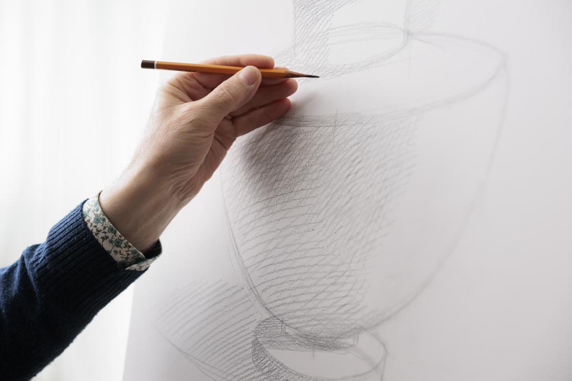 Мужчина затемняет участок рисунка штриховкой, выполненной простым карандашом