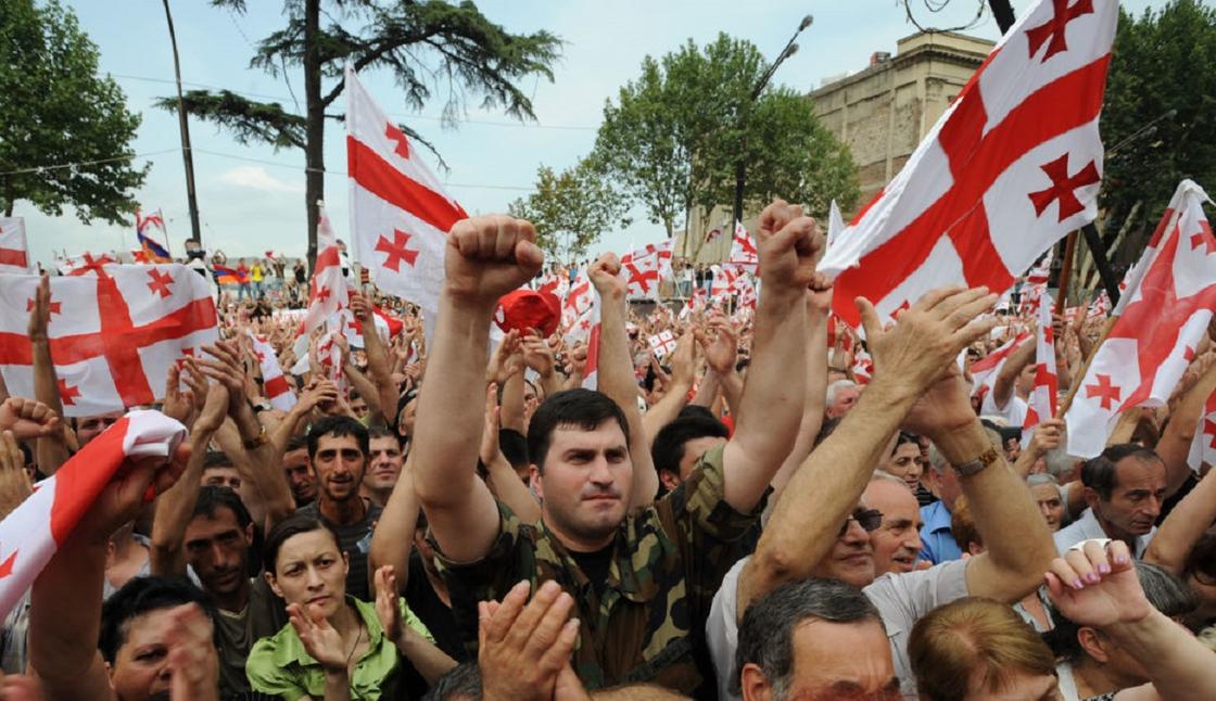 Толпа людей на улице в Тбилиси с флагами Грузии