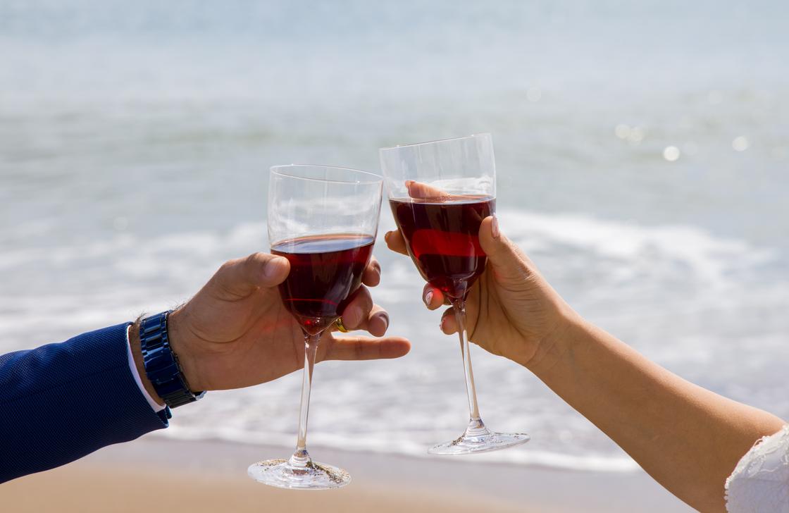 Мужчина и женщина пьют вино из бокалов на фоне моря