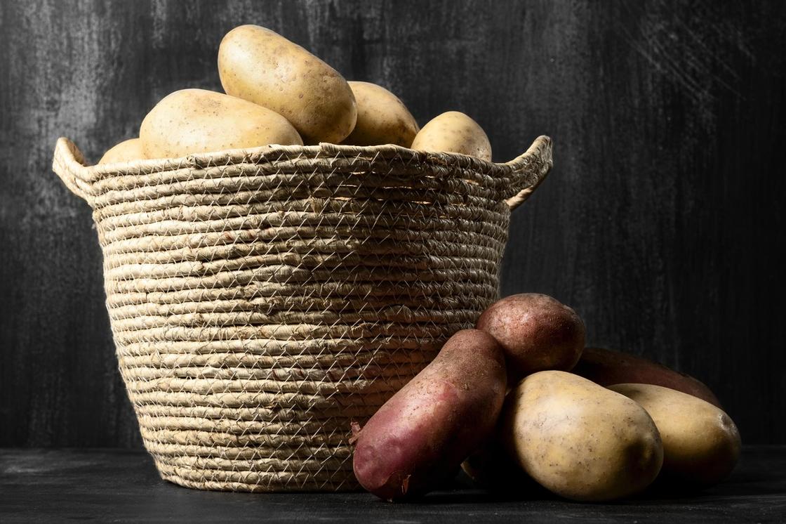 Картофель сложен в плетеную из веревки корзину. Рядом лежит несколько клубней