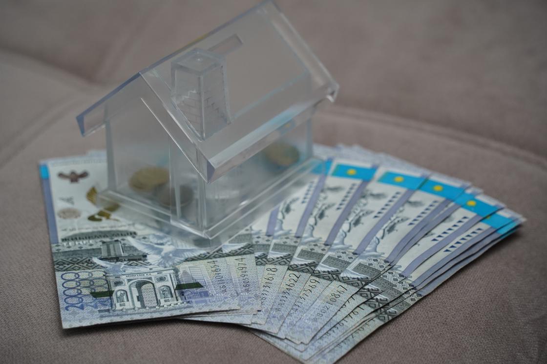 Копилка в виде домика стоит на купюрах тенге