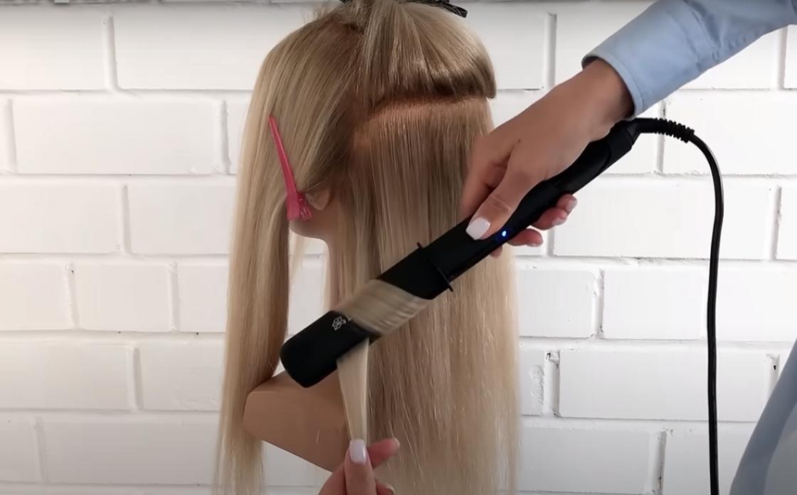 Девушка накручивает волосы на утюжок