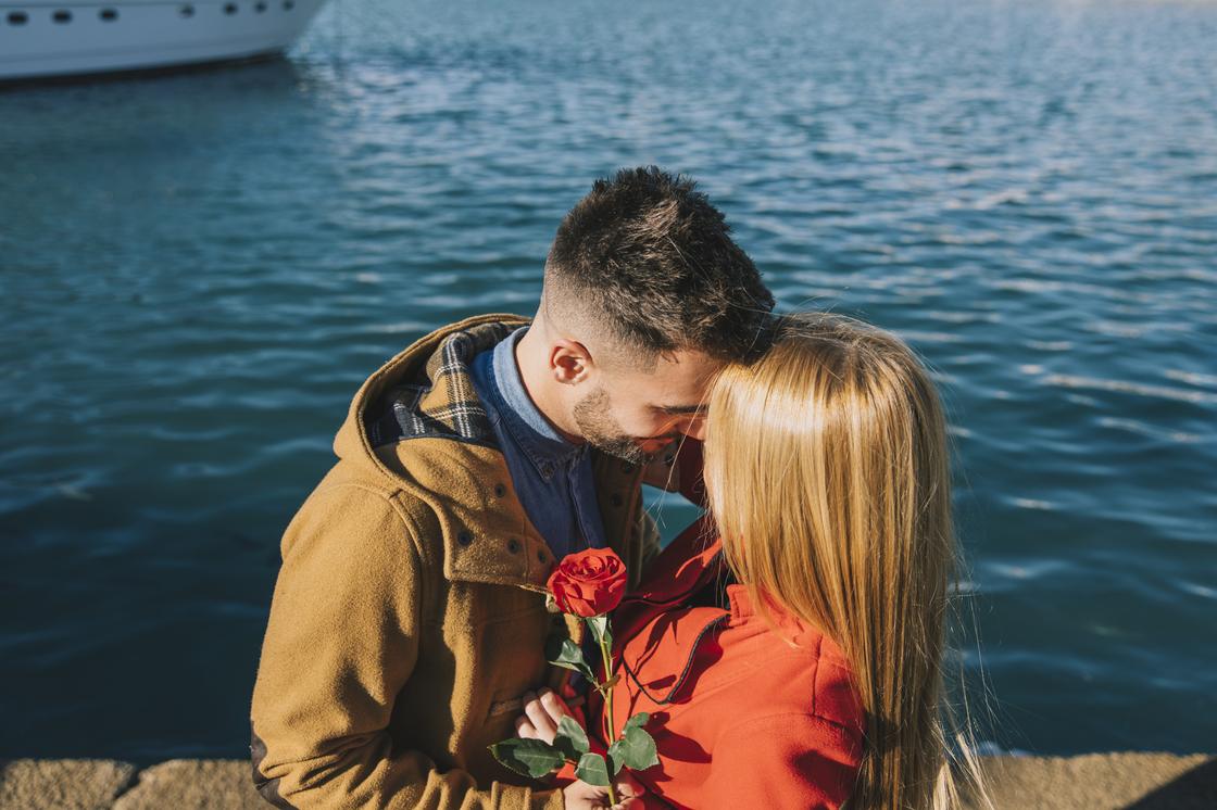 Мужчина обнимает девушку с розой в руках на берегу моря