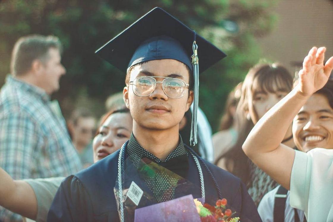 Молодой выпускник колледжа в очках смотрит в камеру