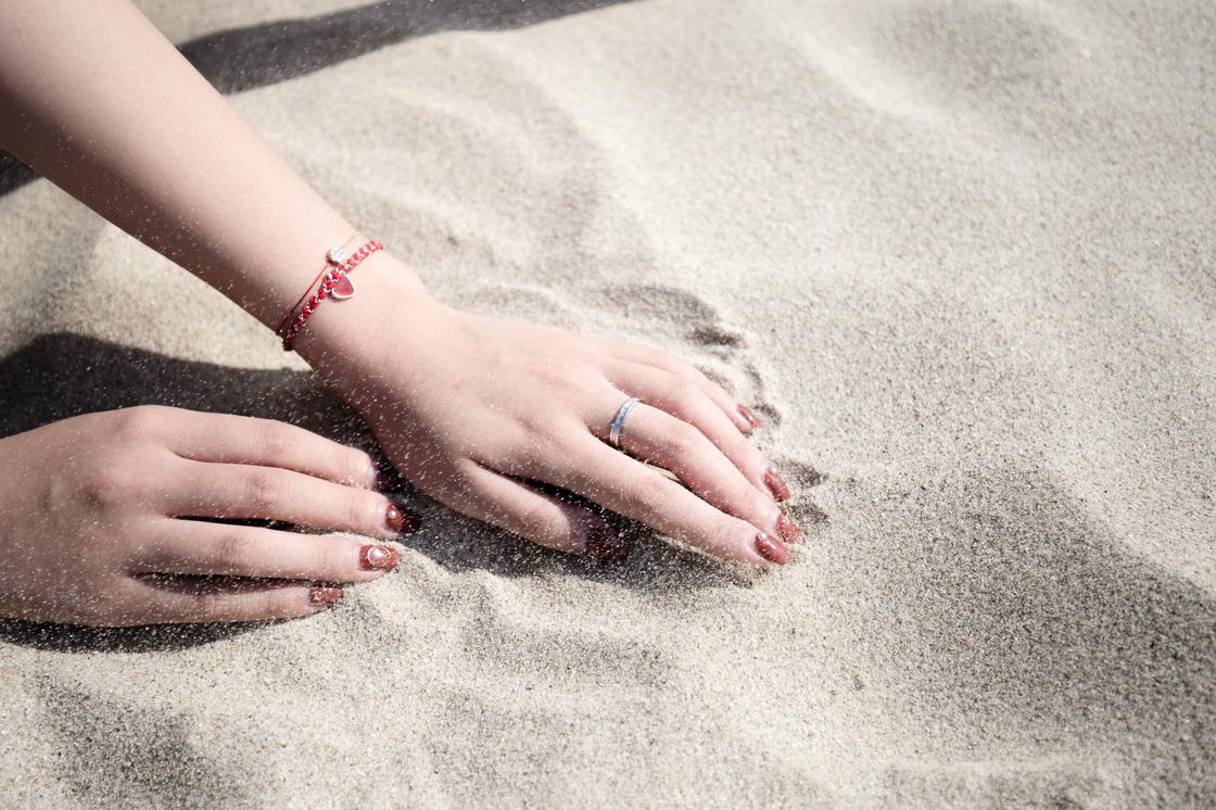 Две руки с браслетами перебирают песок