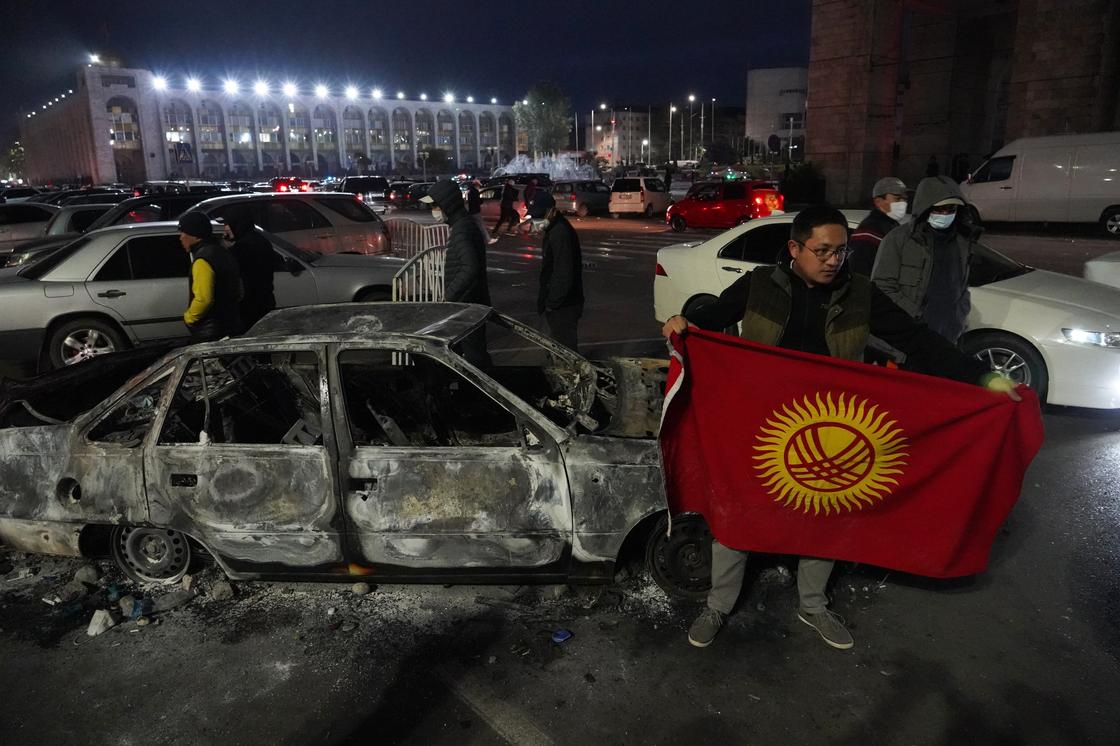 мужчина с флагом перед сгоревшей машиной