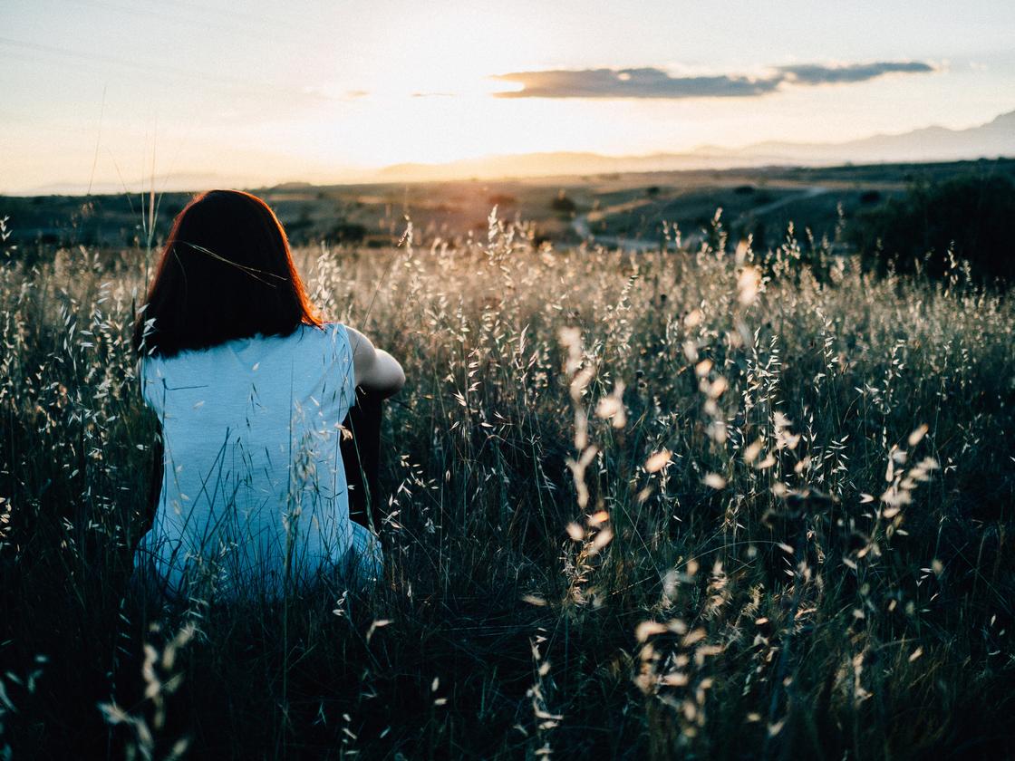 Девушка сидит в поле и смотрит на закат
