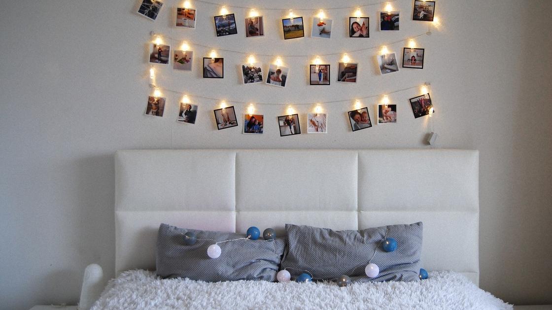 Над кроватью висит гирлянда с лампочками и фотографиями