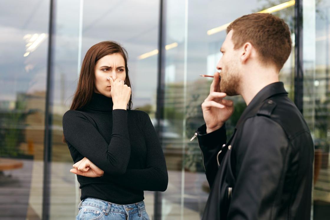 Девушка стоит рядом с парнем, который курит