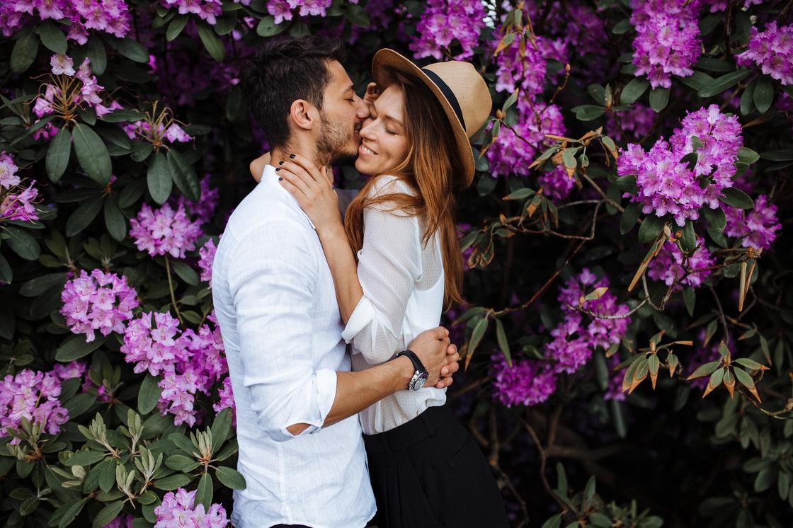 Влюбленная пара обнимается рядом с цветущим кустарником