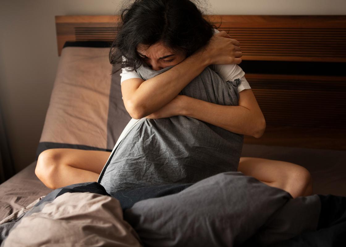 Девушка сидит на кровати, обняв подушку