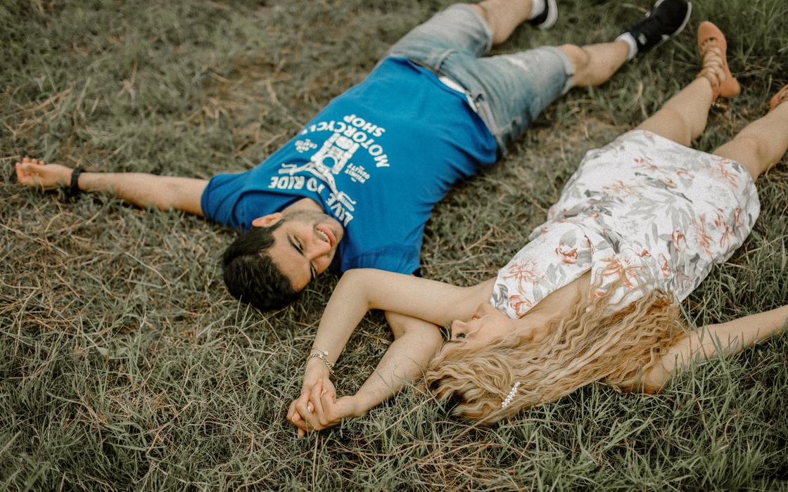 Мужчина и женщина лежат на сухой траве, держась за руки