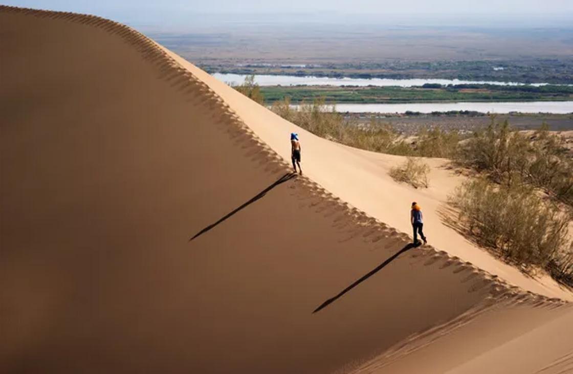 Туристы идут по гребню дюны