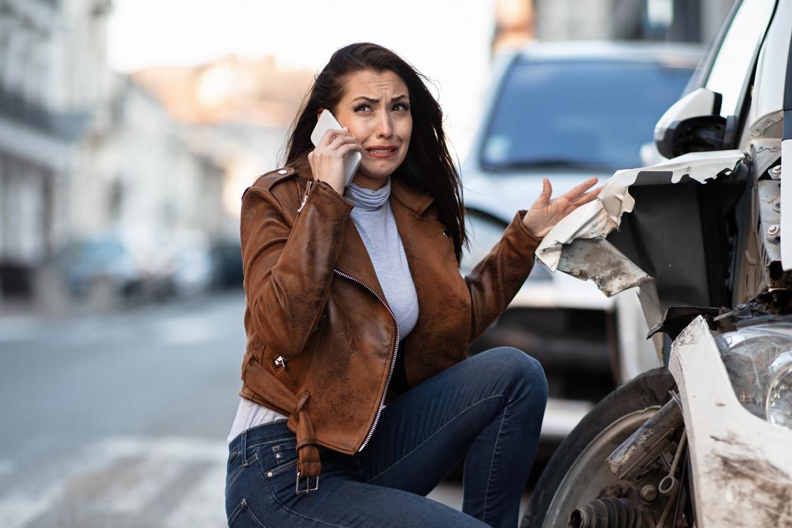 Плачущая девушка говорит по телефону возле разбитого автомобиля