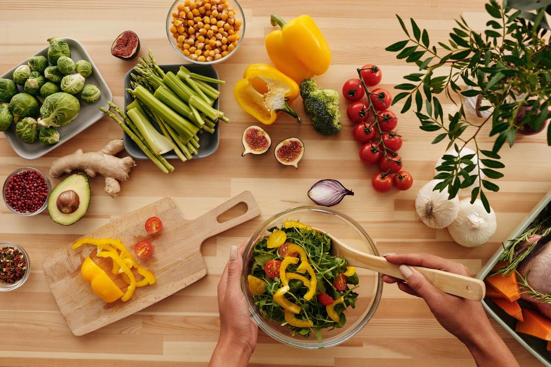 Свежие овощи и фрукты лежат на столе и в тарелках