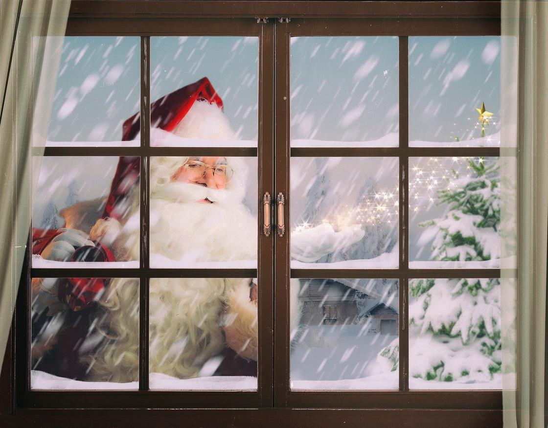 Санта Клаус в очках и красной шапке заглядывает в окно