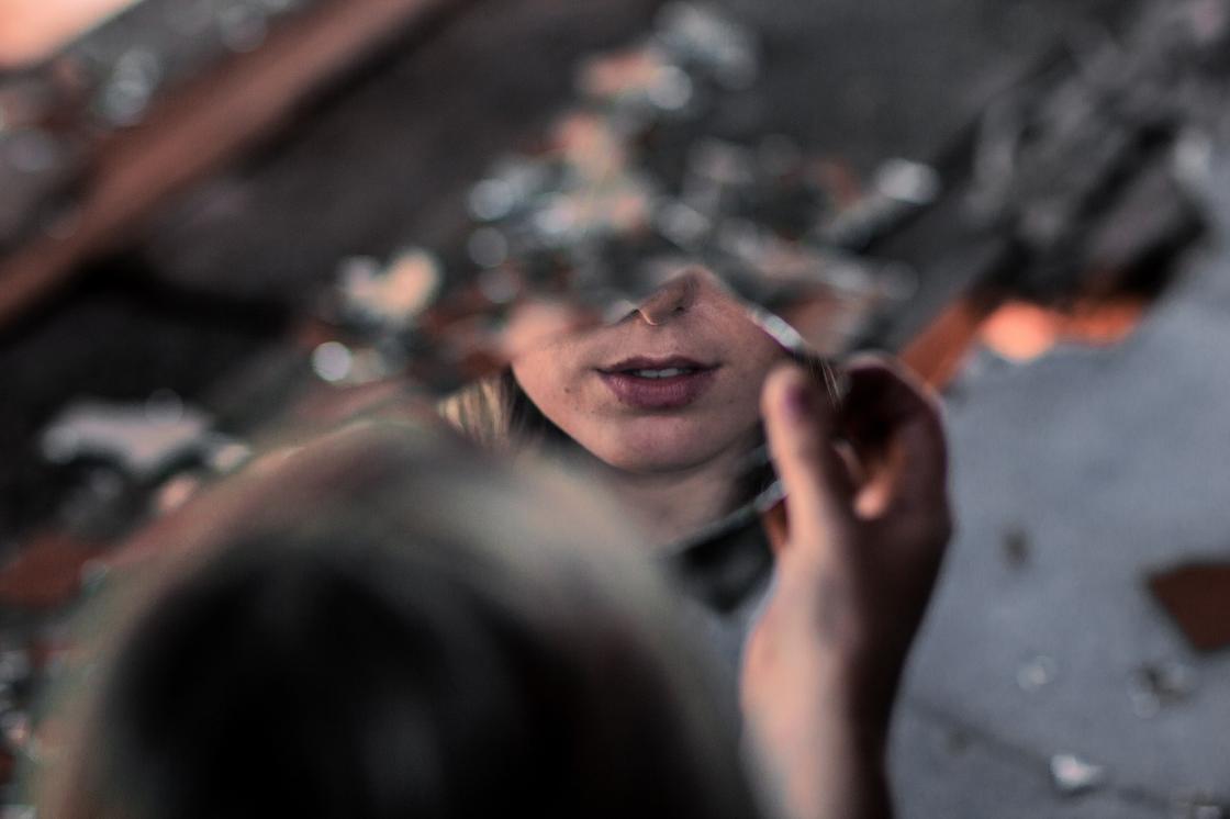 Девушка смотрит в осколок разбитого зеркала
