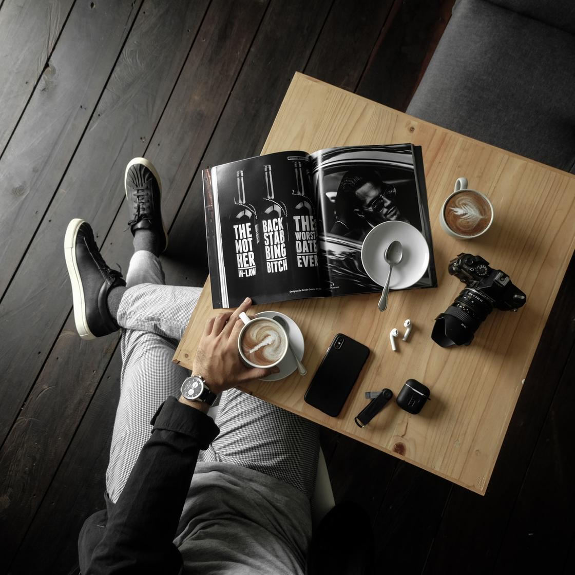 Мужчина, сидящий за столиком с кофе, телефоном и фотоаппаратом