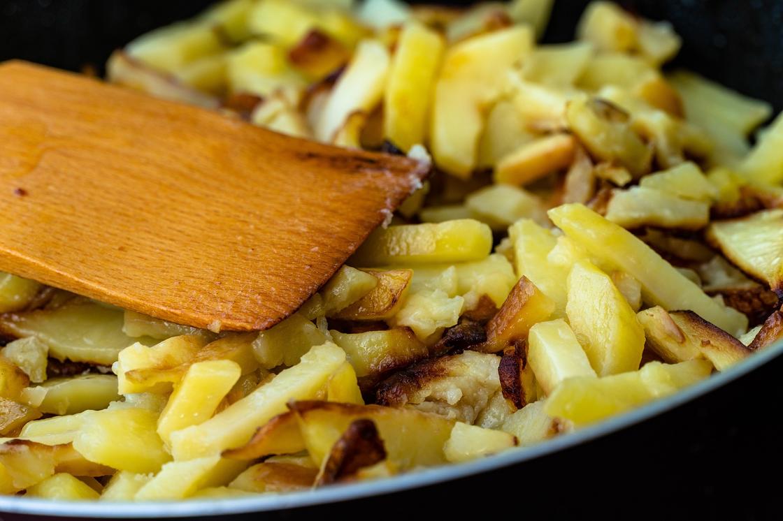 Деревянная лопатка на сковороде с жаренным картофелем
