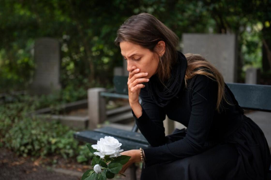 Девушка с белой розой в руках сидит возле могилы