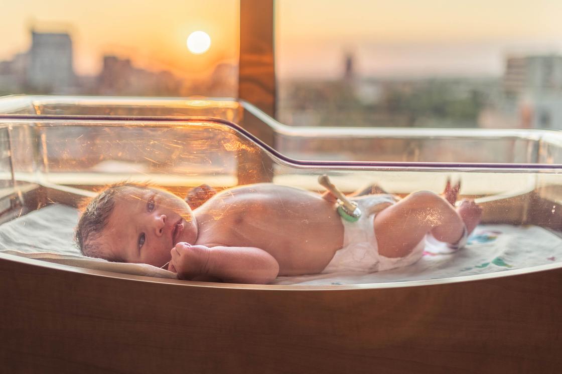 Новорожденный в кроватке на фоне окна