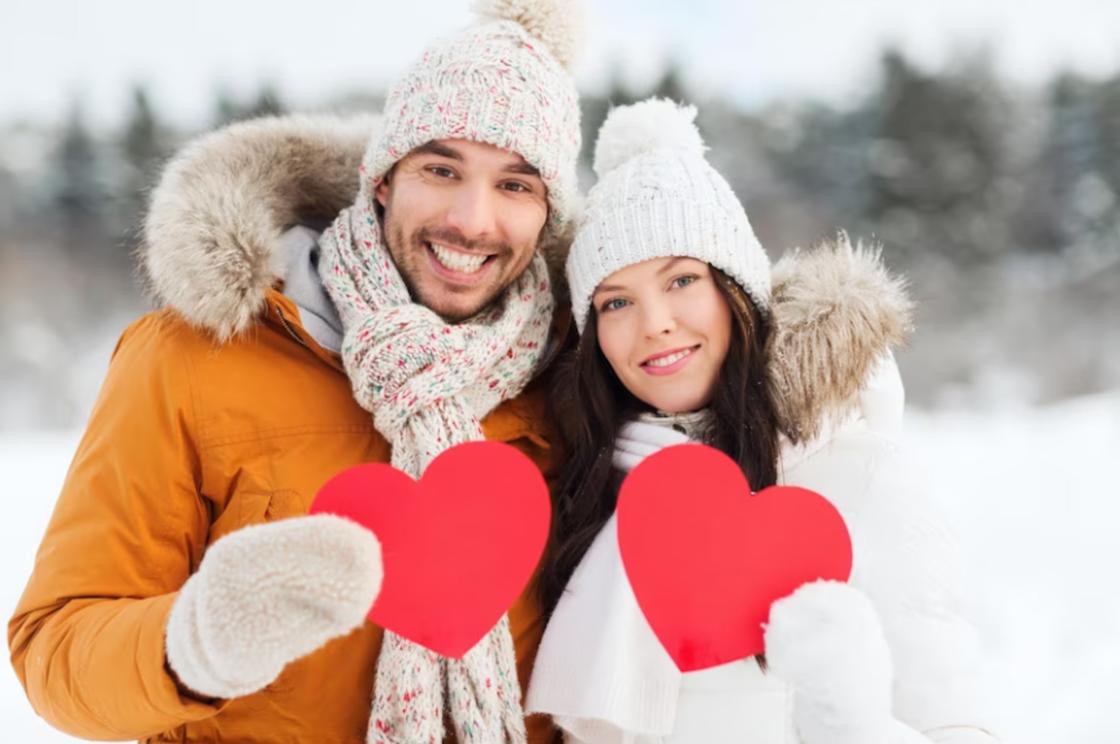 Влюбленная пара держит сердечки на фоне зимнего пейзажа
