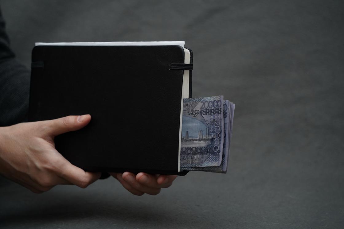 Женщина держит в руках черный блокнот с деньгами