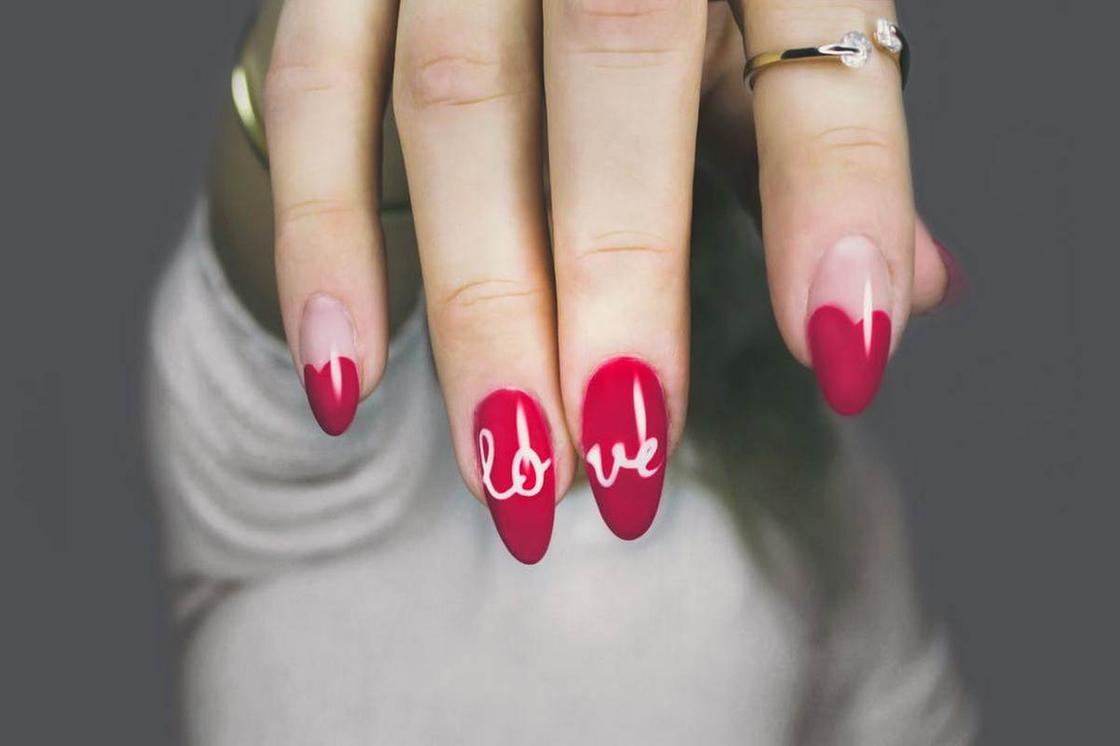 Женская рука с маникюром в красных тонах с англоязычной надписью "любовь"