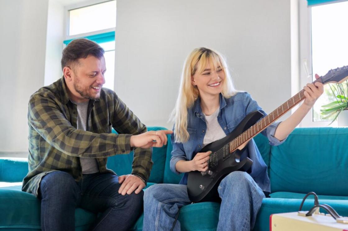 Мужчина учит девушку играть на гитаре