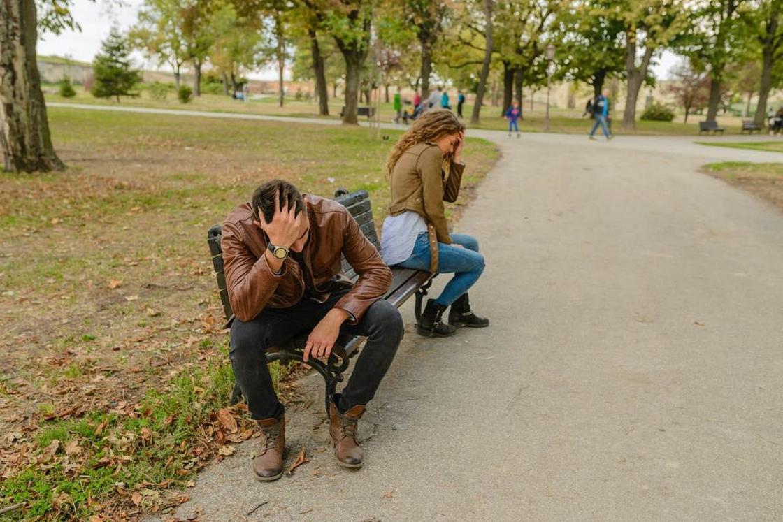 Мужчина и женщина сидят на лавочке в парке, отвернувшись друг от друга