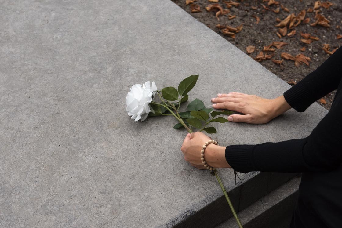 Женщина кладет розу на могильную плиту