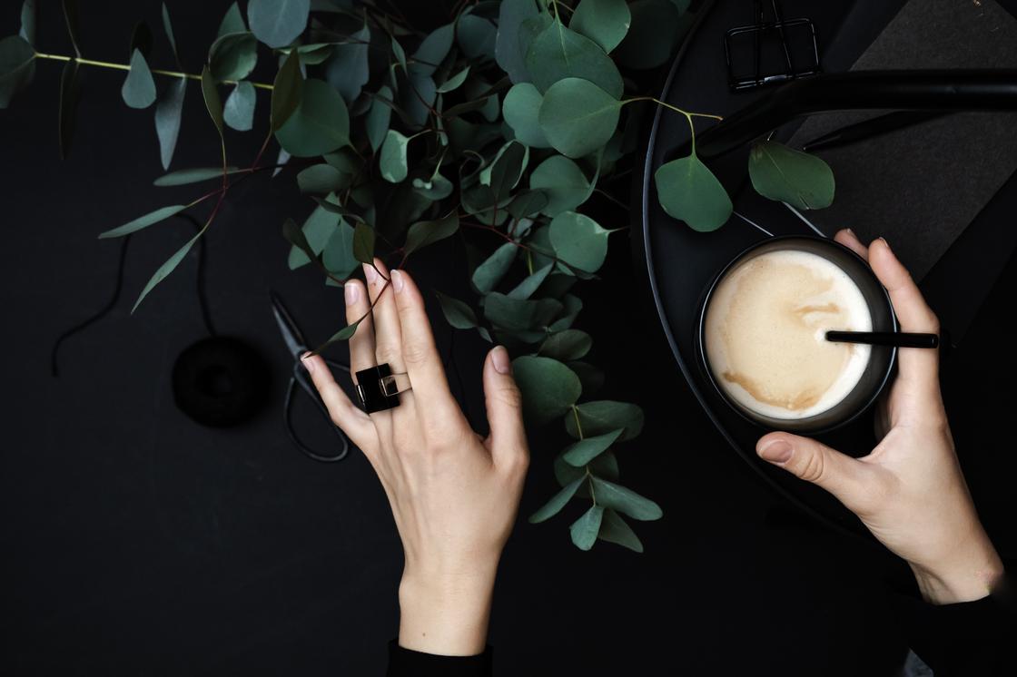 Женские руки и чашка кофе на фоне эвкалиптовых листьев