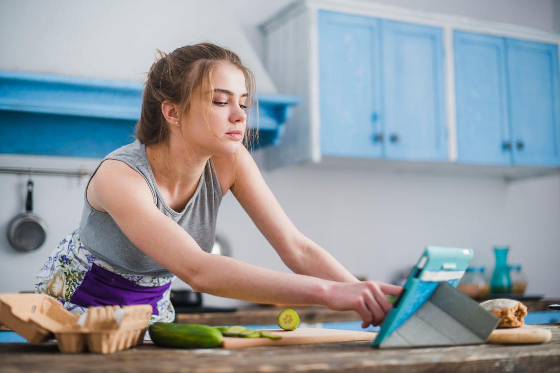 Девушка на кухне ищет рецепт блюда в планшете