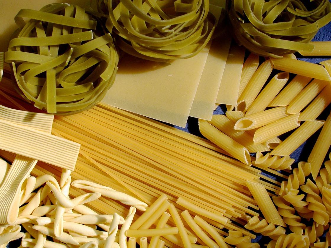 На столе разложены разные виды сухих макаронных изделий: перья, спагетти, лапша, спиральки