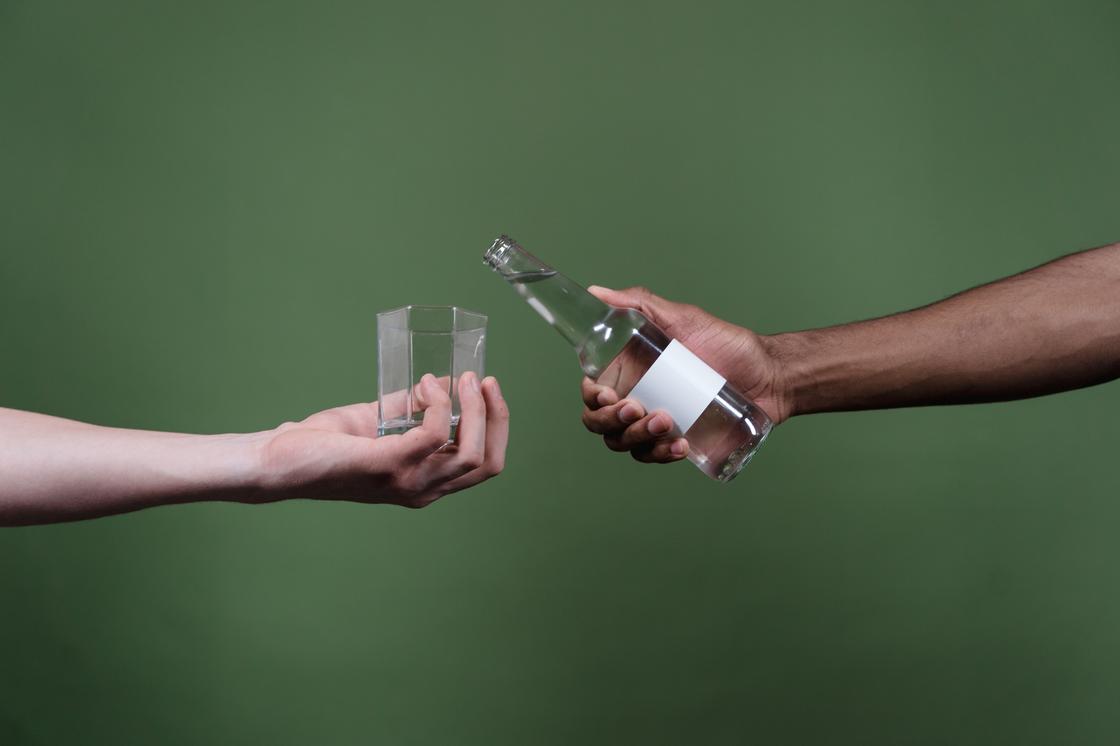 Бутылка с водой и пустой стакан в руке