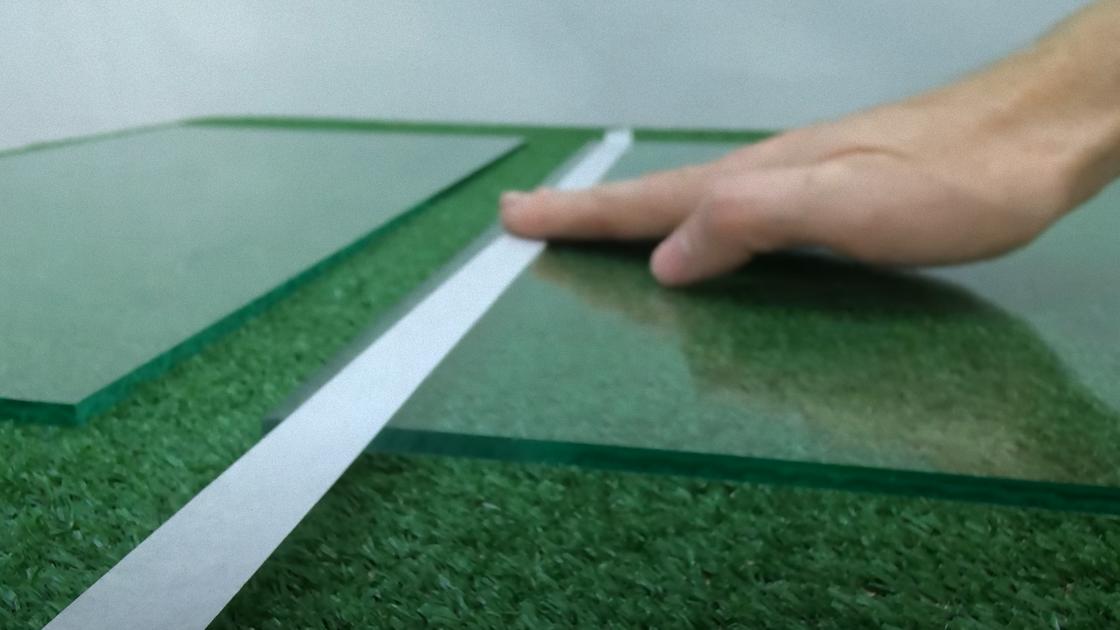 На зеленой поверхности лежат куски толстого стекла. По краю стекла клеят белую ленту