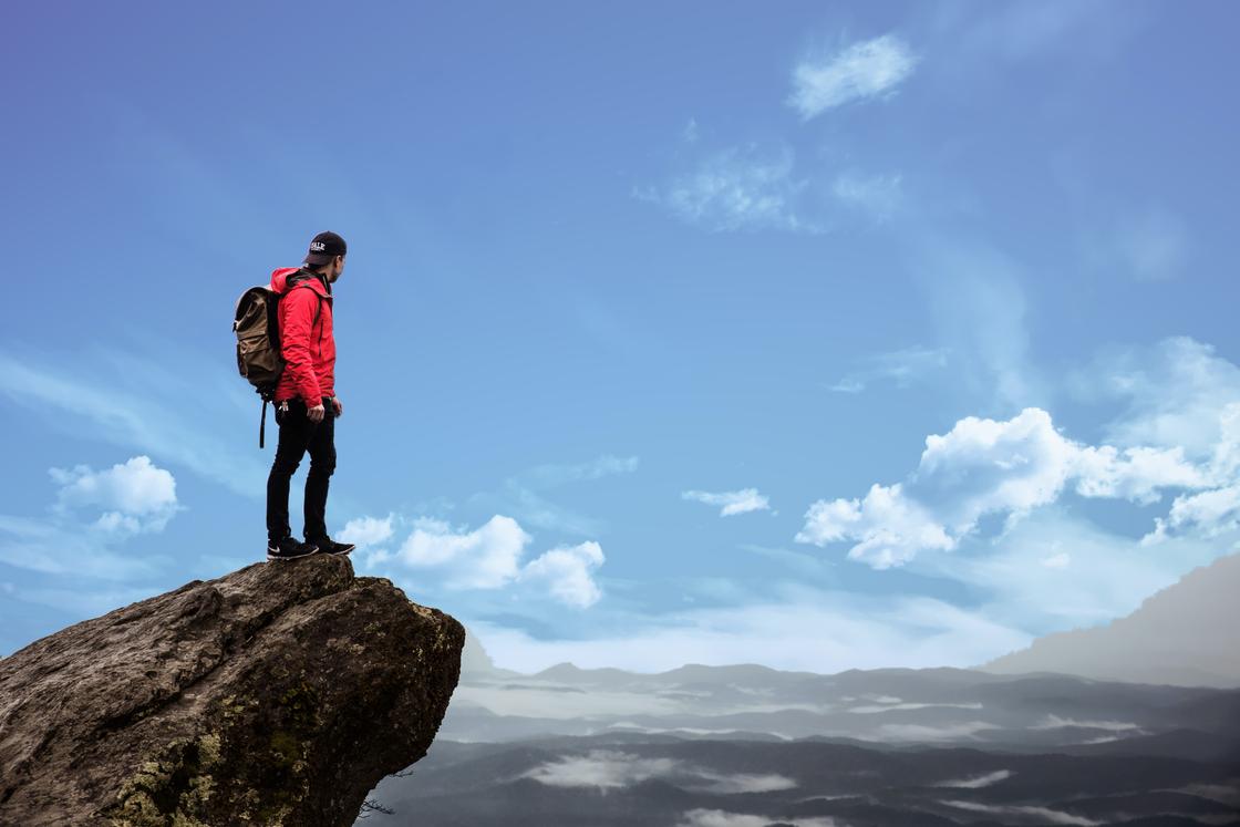 Человек стоит на скале и смотрит на горы