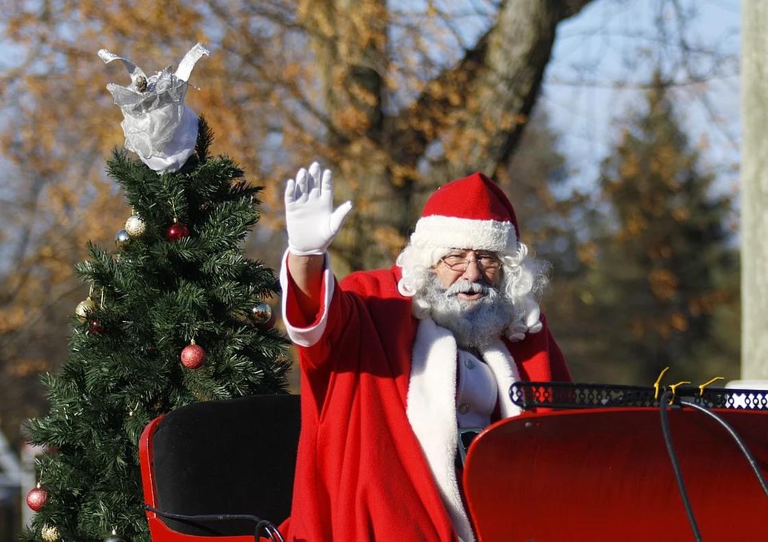 Санта-Клаус в санях по улице  машет рукой