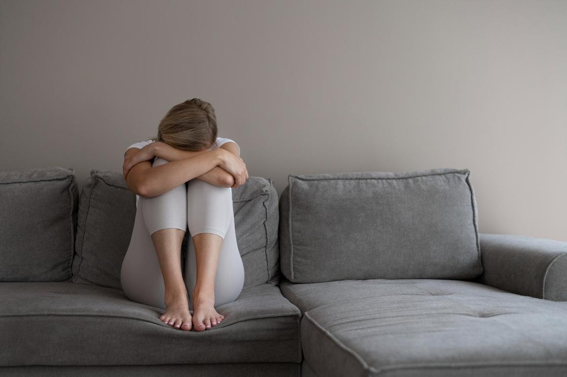 Девушка сидит на диване, обняв руками колени
