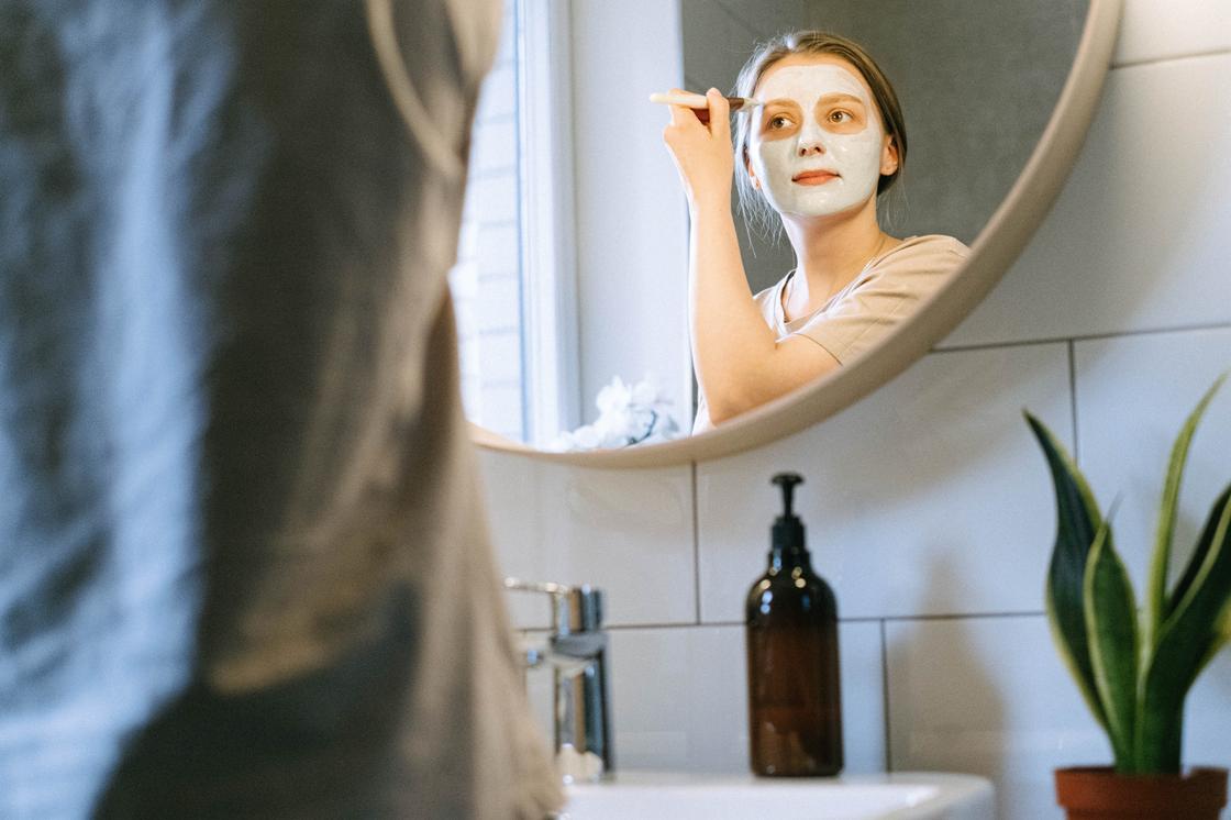 Девушка наносит косметическую маску перед зеркалом