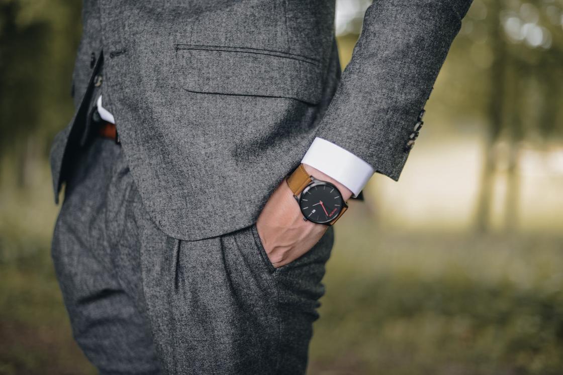 Мужчина в деловом костюме сует руку с наручными часами в карман