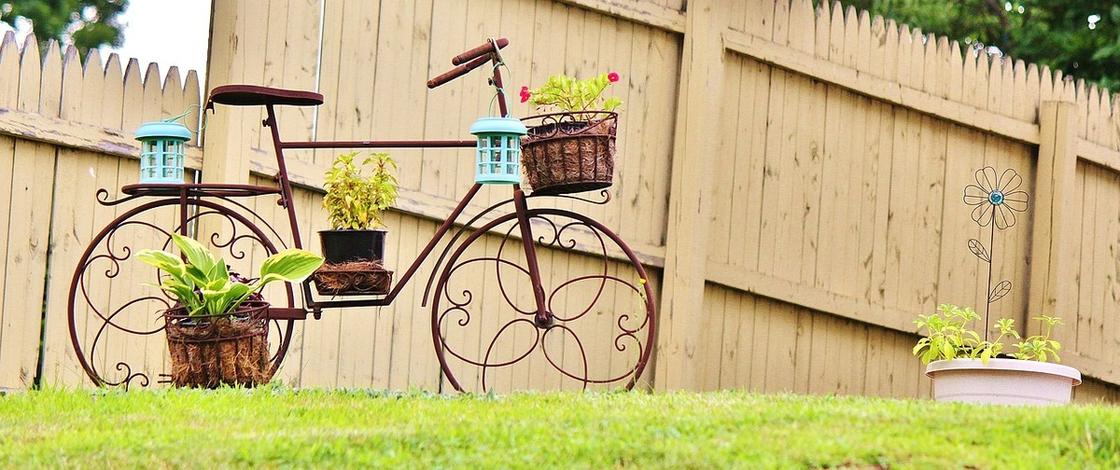 Велосипед с прикрепленными корзинами для цветов установлен на лужайке возле высокого деревянного забора
