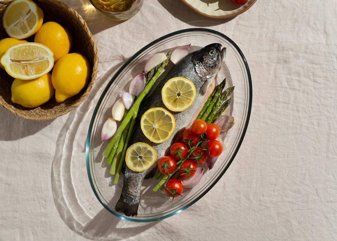 Свежая форель в миске с лимоном, чесноком и помидорами