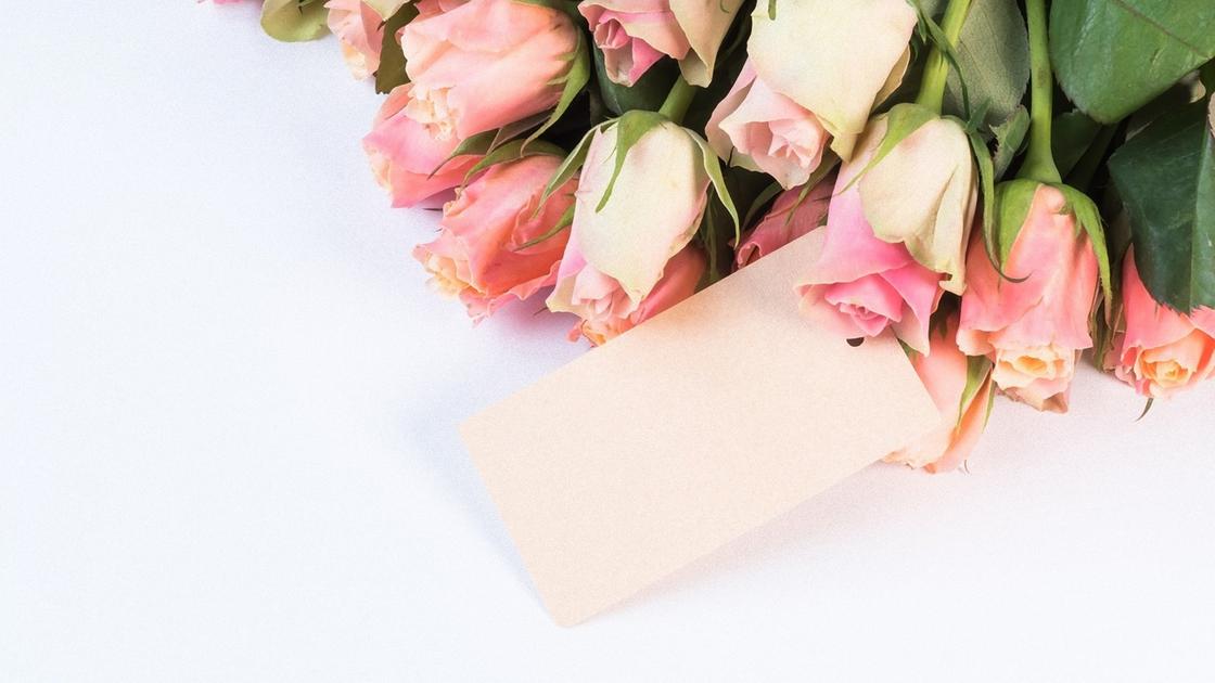 Розовые розы лежат на столе с конвертом