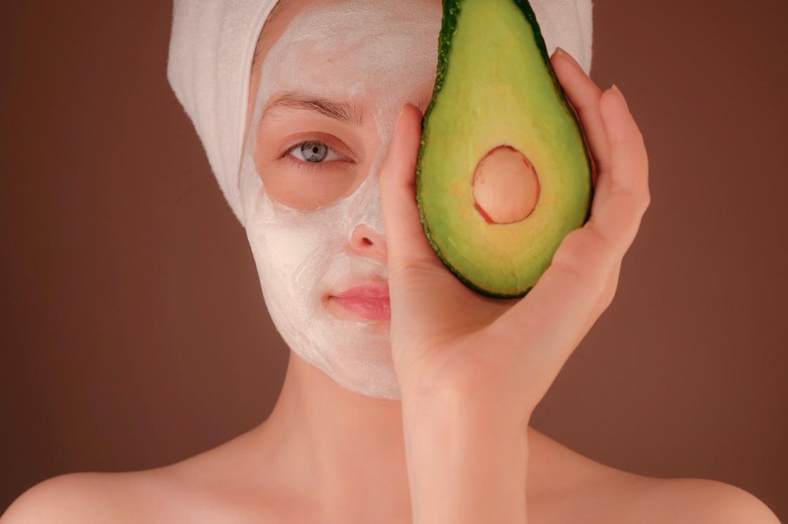 Девушка в косметической маске держит в руке авокадо