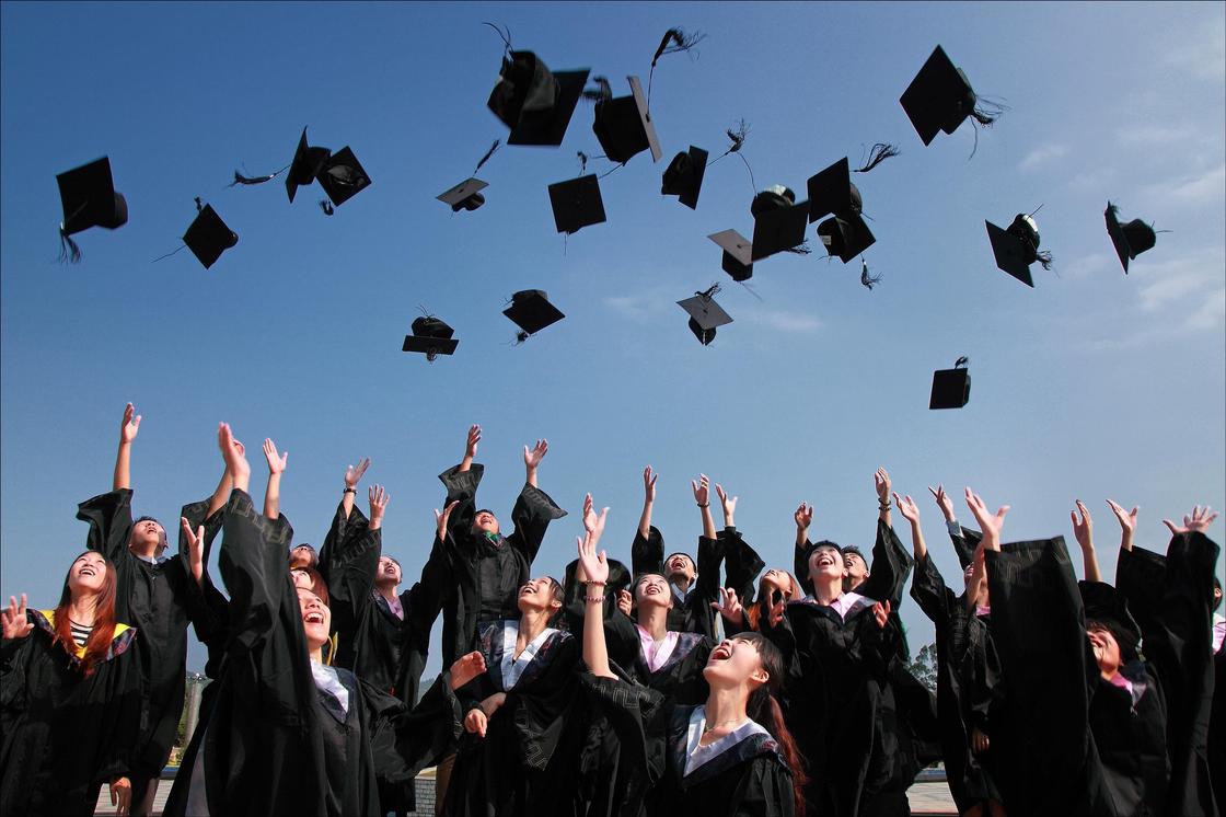 Подростки подбрасывают вверх шапочки выпускников