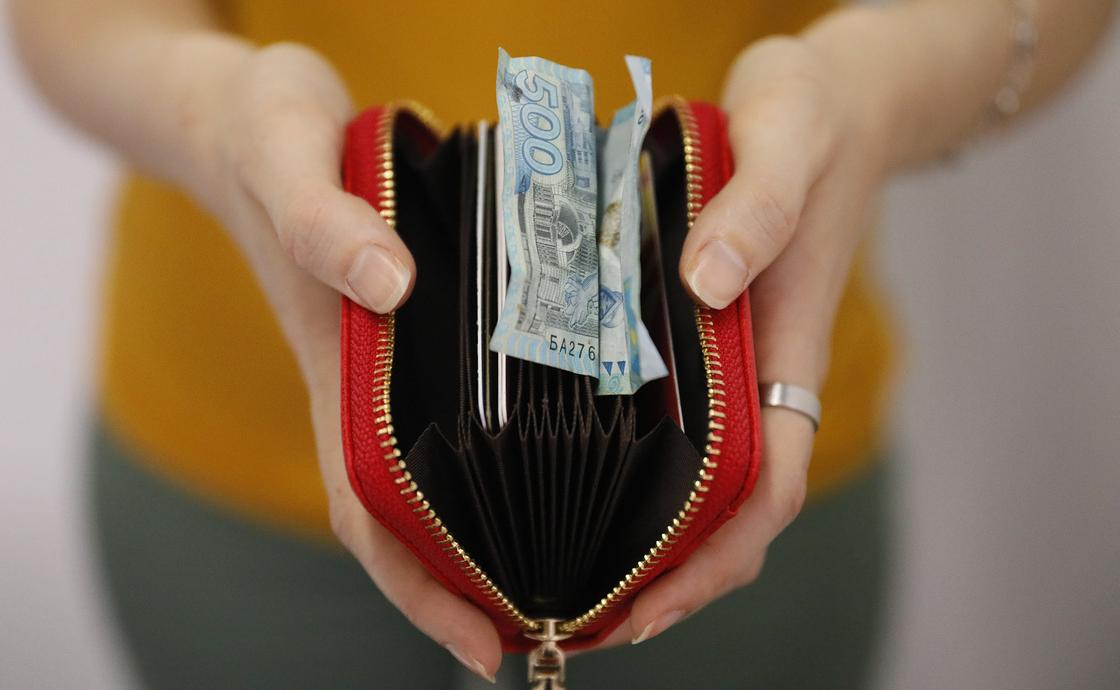 Девушка держит в руках кошелек с комканной купюрой 500 тенге